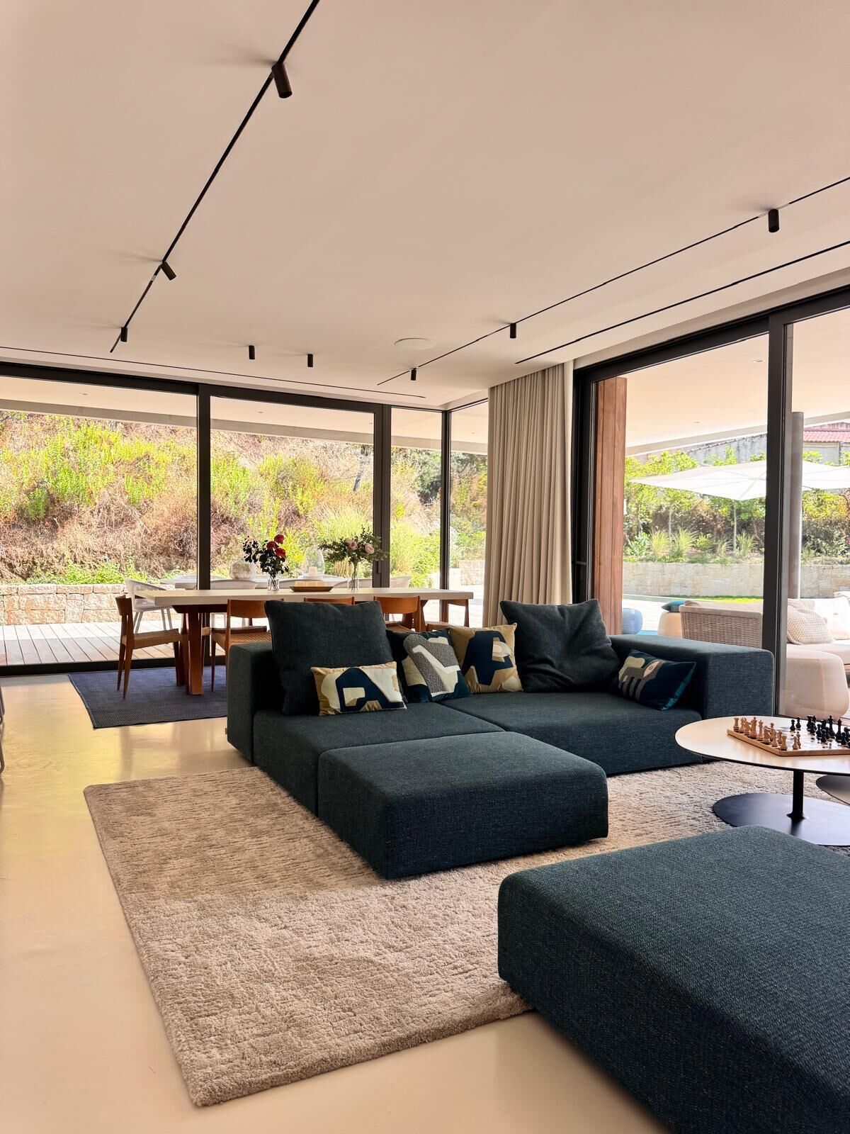 Un salon moderne doté d’un canapé d’angle, d’un coin repas et de grandes fenêtres offrant une vue sur la verdure.