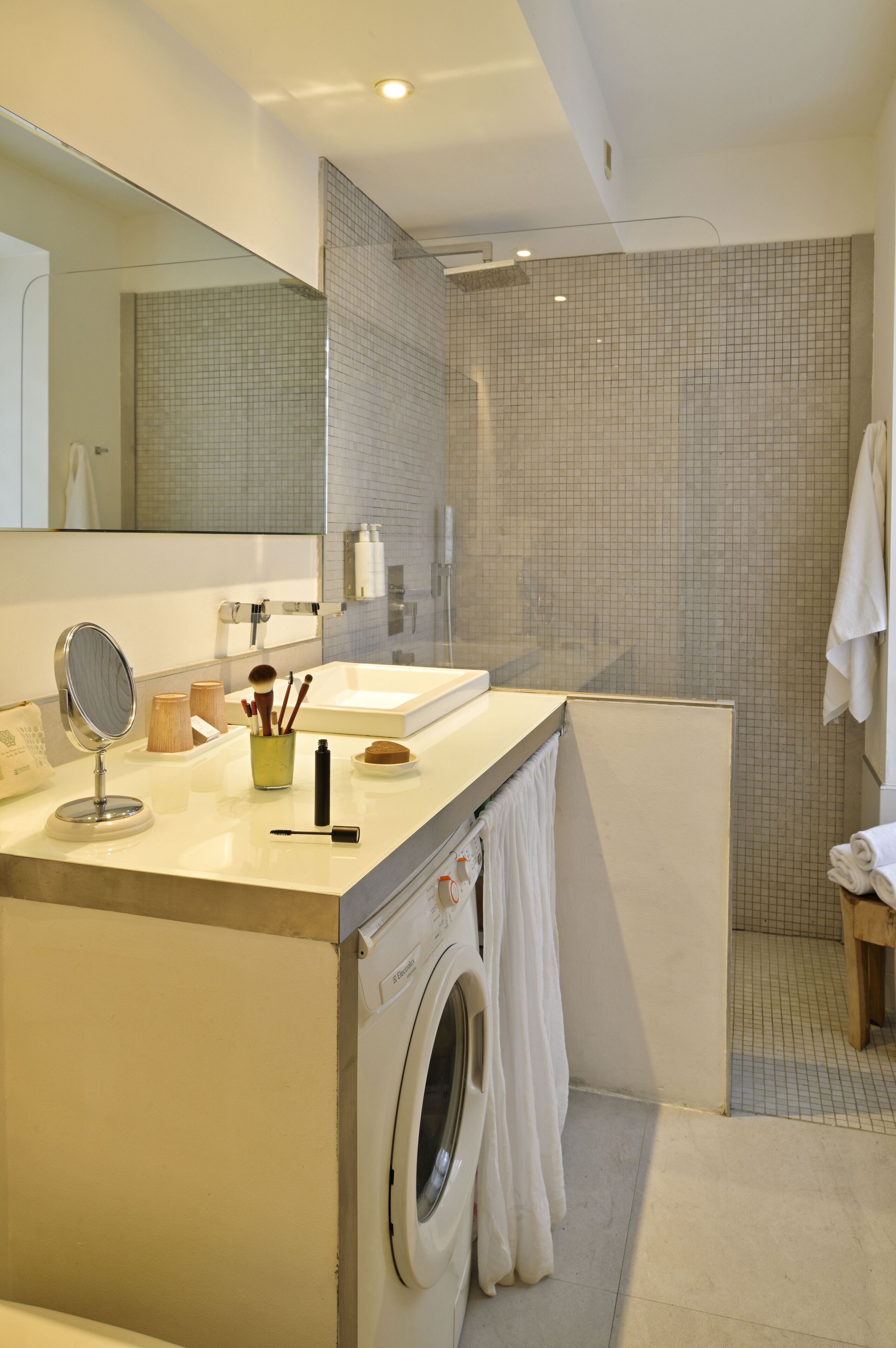A modern bathroom with a built-in washing machine, a large mirror, and a shower area.