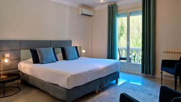Un dormitorio moderno con una cama grande, una mesita de noche con lámpara, una silla y vistas al verdor por la ventana.