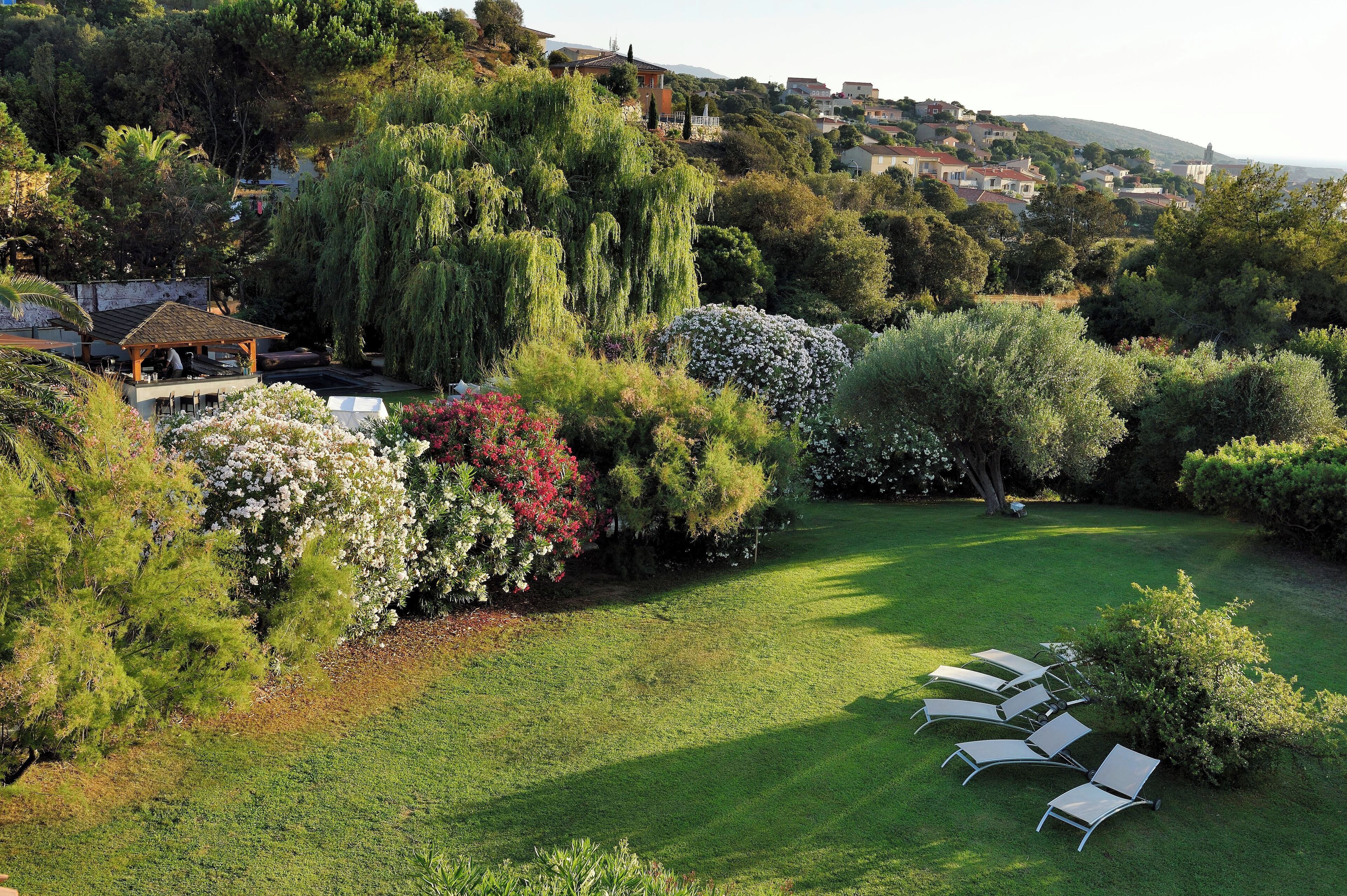 A lush garden with a gazebo, a well-manicured lawn, and a row of white lounge chairs.