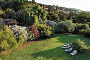 Un exuberante jardín con un pabellón, césped impecable y una fila de sillones blancos.