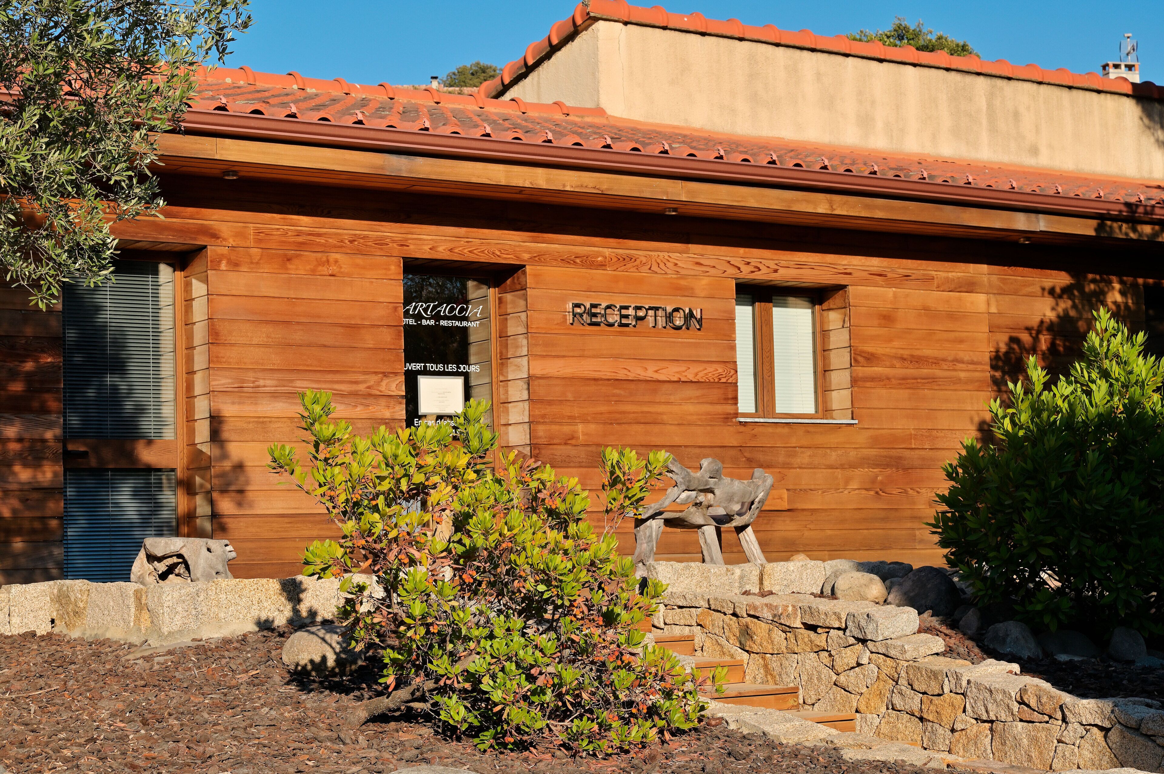 A wooden building with a reception area, stone steps, and a small statue.