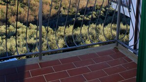 Ein Balkon mit Metallgeländer, der auf eine hügelige Landschaft mit Vegetation und ferner Hügeln blickt.