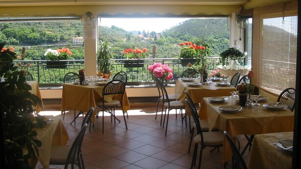 Ein Restaurant mit Außenbereich und Blick auf eine reizvolle Landschaft. Die Tische sind mit Tellern, Gläsern und Besteck gedeckt.