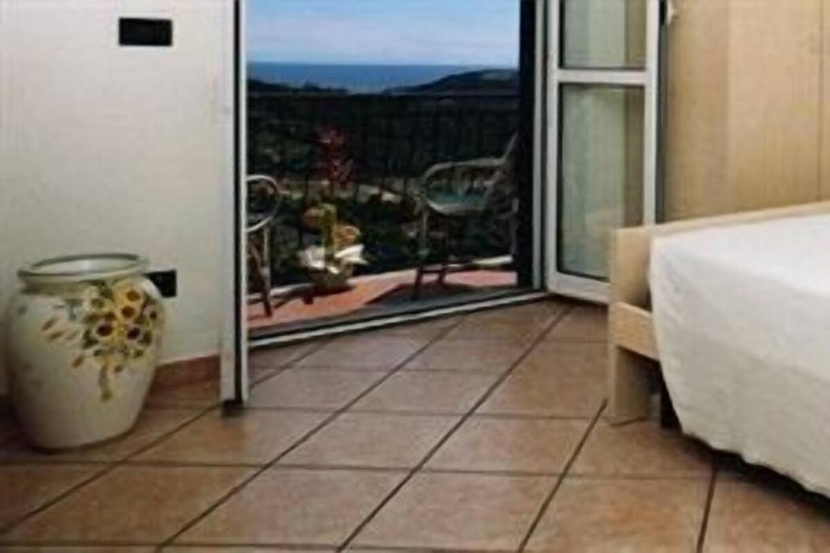 Una camera da letto con un letto, vista tramite una porta vetrata e pavimento piastrellato.