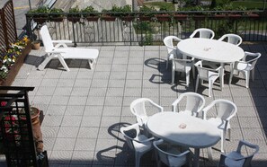 An outdoor patio with white plastic furniture, including a round table and chairs, and a sun lounger. - Albergo Da Cecilia (Bognanco)