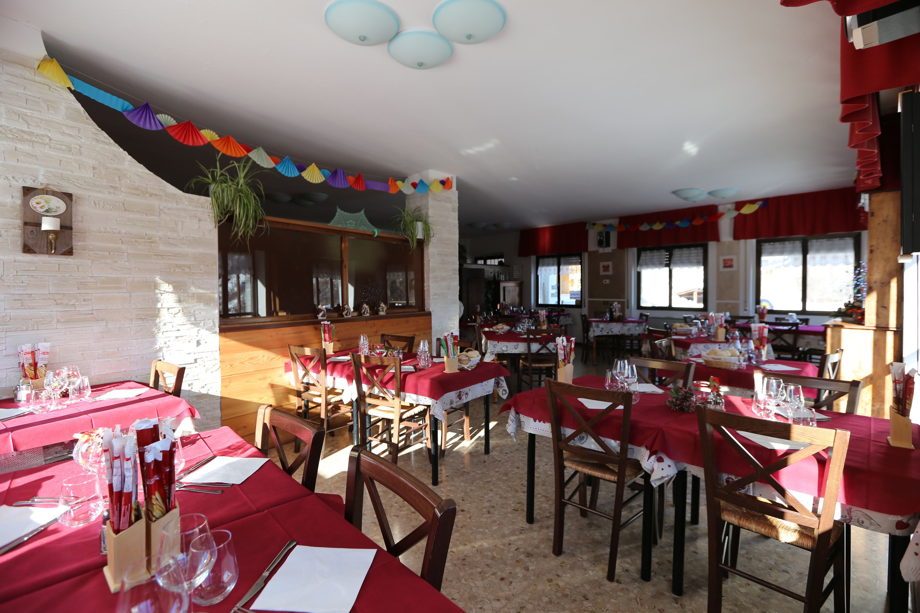 Un restaurante con varias mesas cubiertas con manteles rojos, sillas de madera y una pared de ladrillo.
