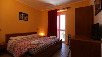 Ein Hotelzimmer mit Bett, Schreibtisch, Fernseher und einem Fenster mit Vorhängen.