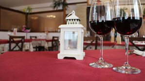 A dining table with two wine glasses filled with red wine, a white lantern, and a red tablecloth. - Albergo Da Cecilia (Bognanco)
