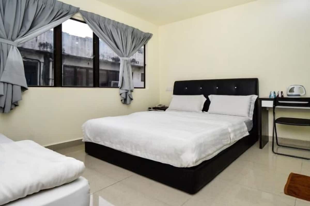 A hotel room with a single bed, a desk with a chair, and a window with curtains.