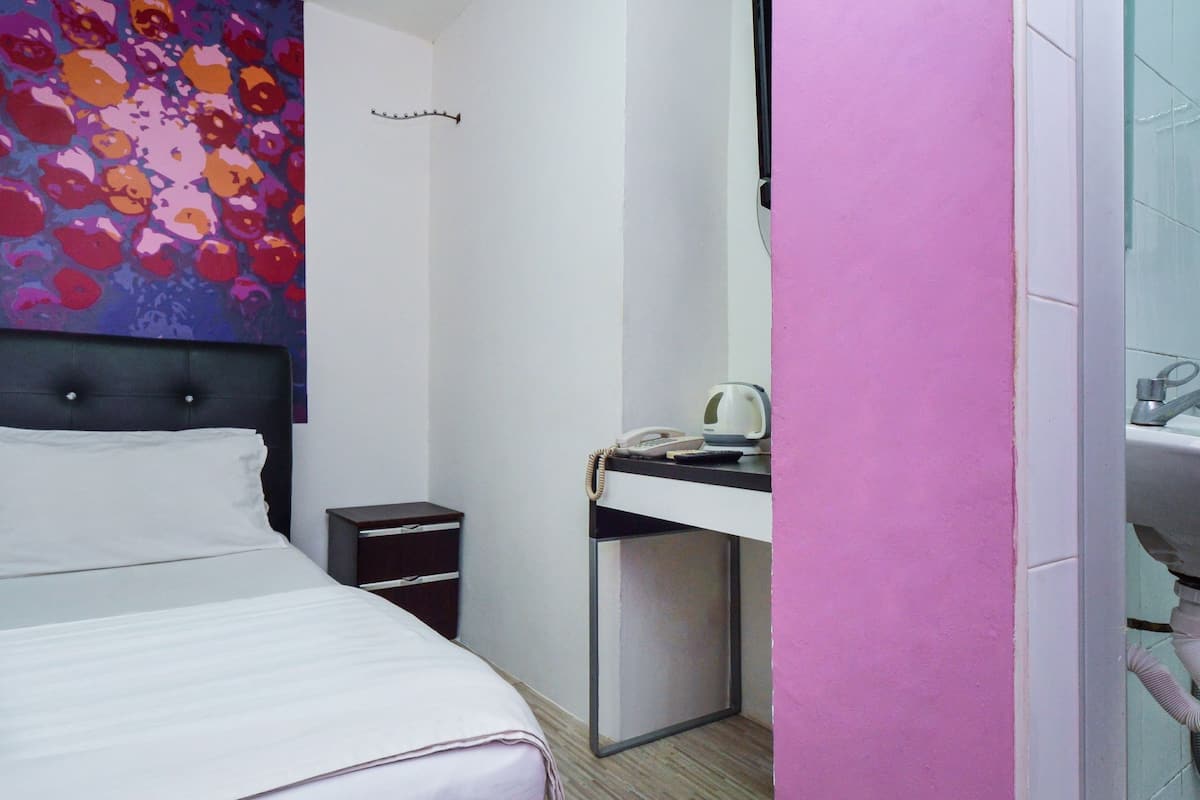 A hotel room with a bed, a bedside table, a desk with a telephone and a kettle, and a bathroom with a sink.