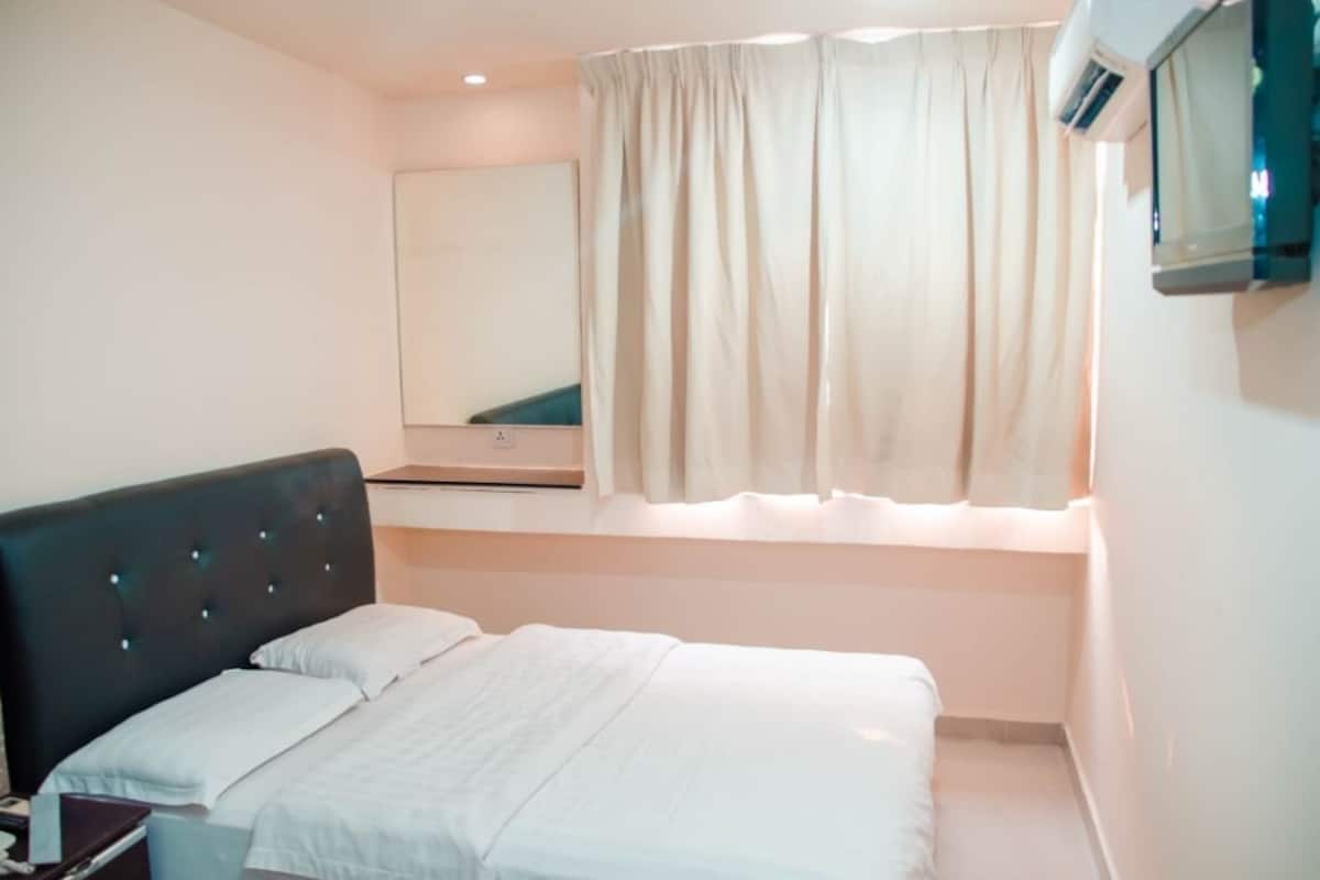 A bedroom with a bed, a nightstand, a mirror, and a window with curtains.