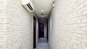 Un pasillo estrecho con paredes de ladrillo blanco, un ventilador de techo y un equipo de aire acondicionado.
