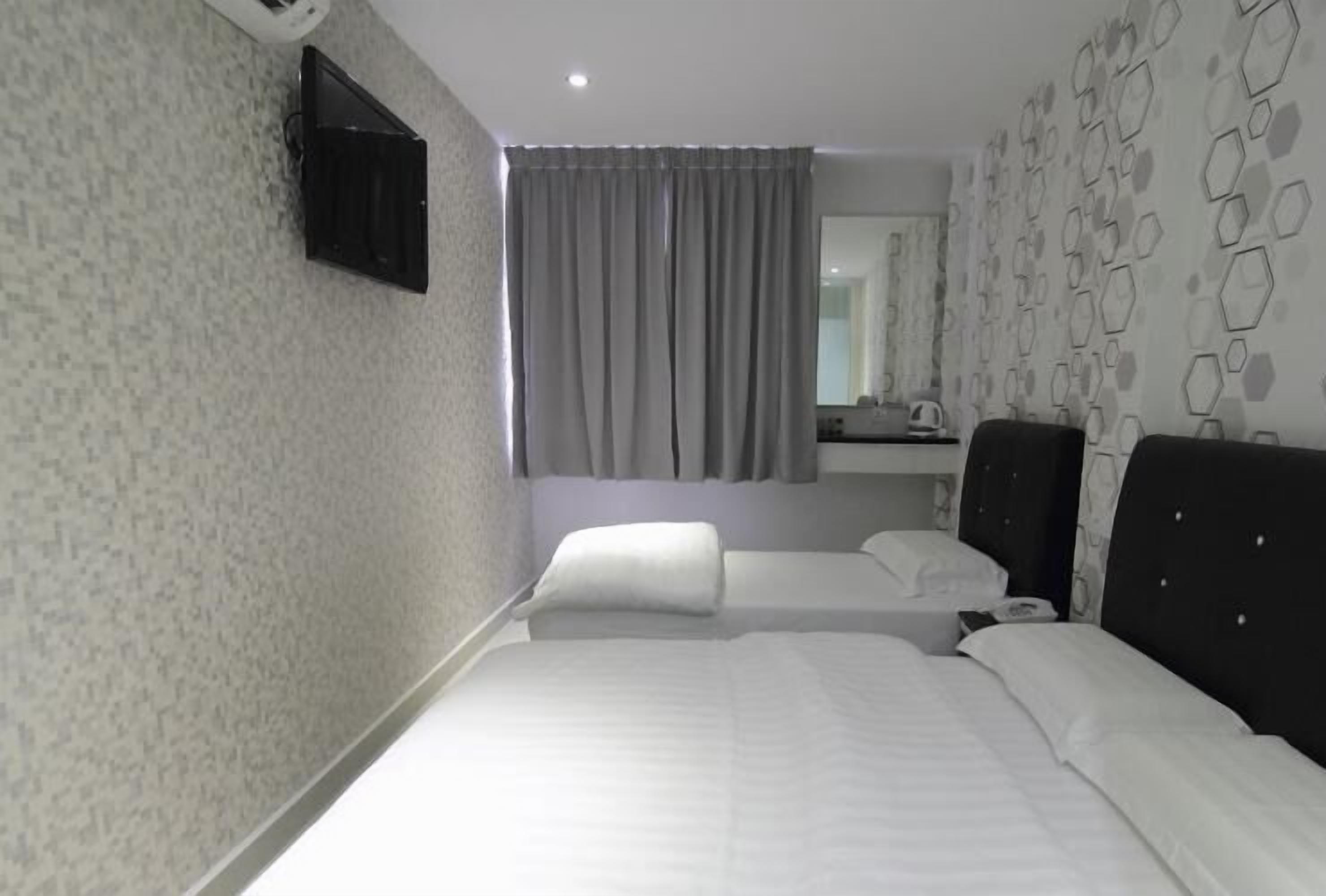 A hotel room with two beds, a flat-screen TV mounted on the wall, a bathroom mirror, and a patterned wall.