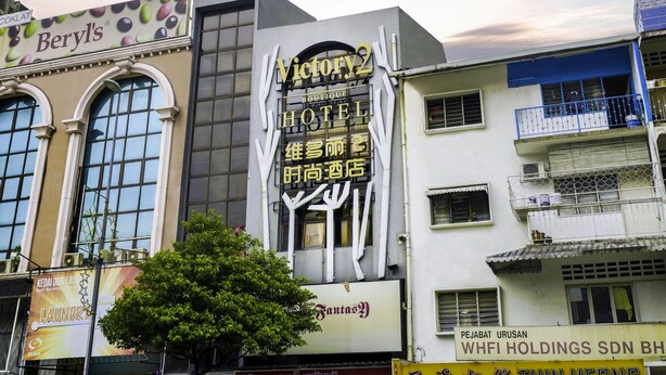 Un hotel con un cartel llamativo en varios idiomas, amplias ventanas y un árbol en la fachada.