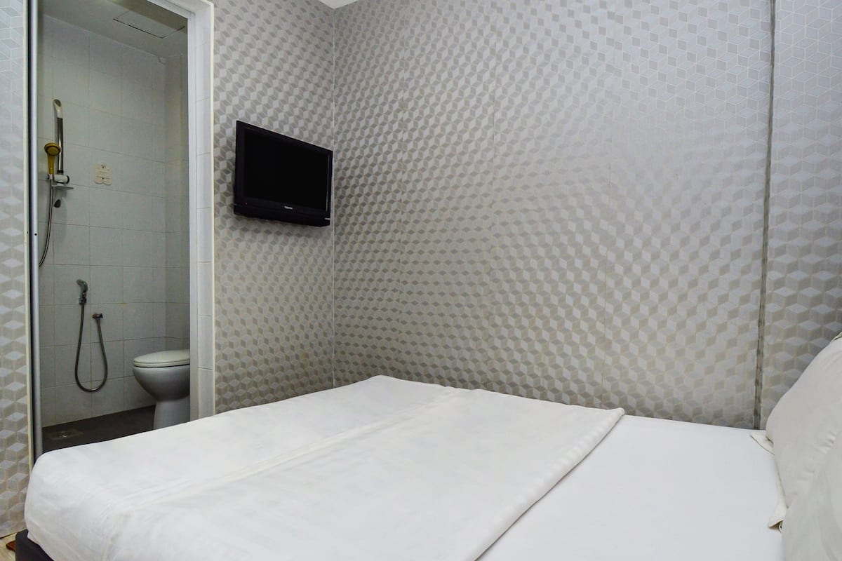 A hotel room with a bed, a television mounted on the wall, and a shower area with a toilet.