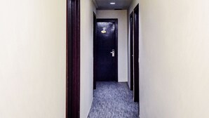 Un pasillo estrecho con suelo alfombrado, una puerta oscura al final e interruptor de luz en la pared.
