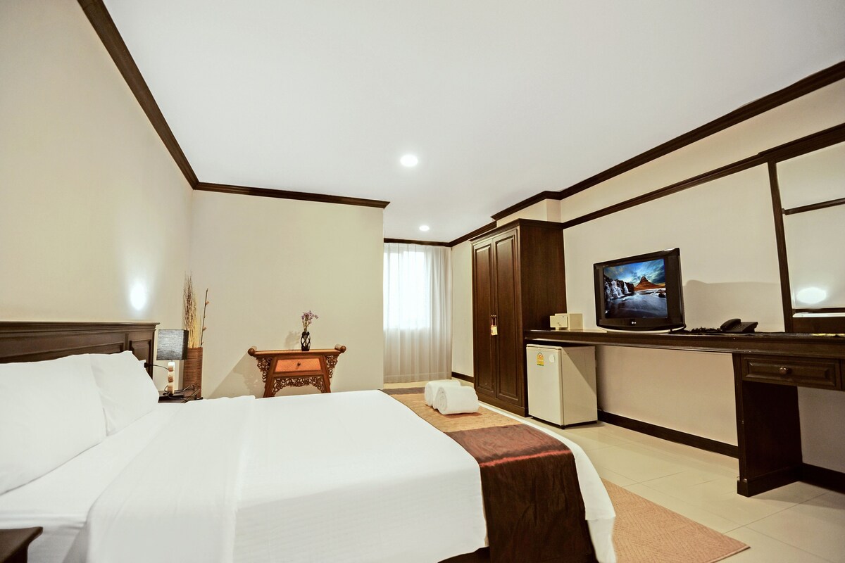A hotel room with a bed, desk, television, and a small refrigerator.