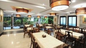 Ein Restaurant mit mehreren Tischen und Stühlen, großen Hängelampen und großen Fenstern mit Blick auf Grünflächen.