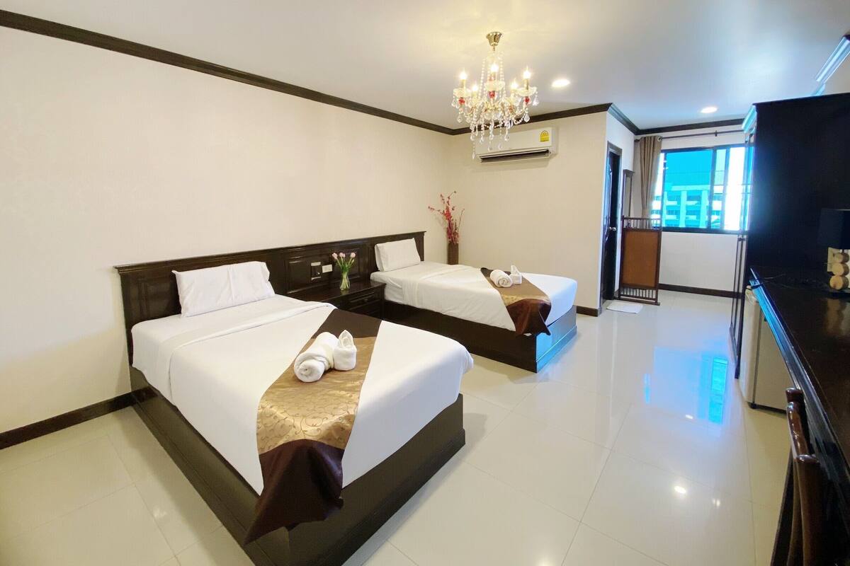 A hotel room with two beds, a chandelier, an air conditioning unit, and a television.
