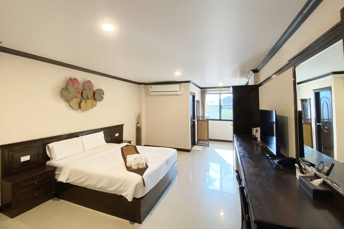 A modern hotel room with a large bed, a flat-screen TV, a desk with a chair, and a large window offering a view of the city.