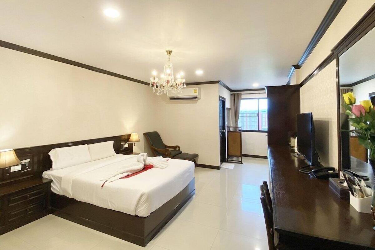 A hotel room with a bed, a desk, a chair, a TV, and a chandelier.
