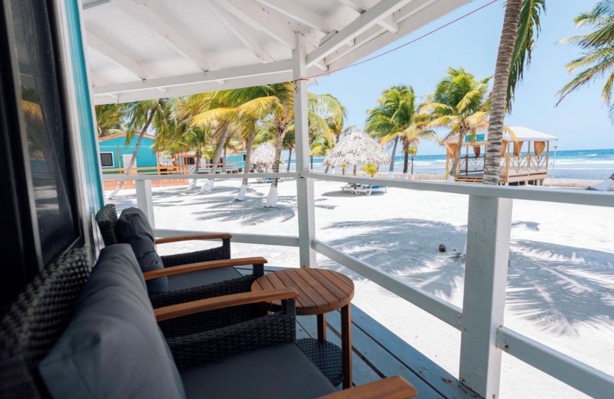 Un espacio de estar al aire libre cubierto con vistas a una playa y palmeras.