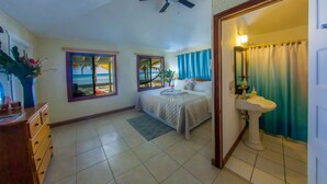 Une chambre à coucher comprenant un lit, une commode, une fenêtre avec vue, un ventilateur de plafond et une salle de bain avec un lavabo et un miroir.