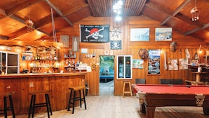 Un espace bar avec des murs en bois, une table de billard et un comptoir avec des tabourets.