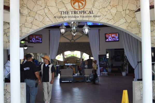 An entrance to The Tropical at Lifestyle Holidays Vacation Resort with a stone archway, two televisions, and a seating area with a bar.