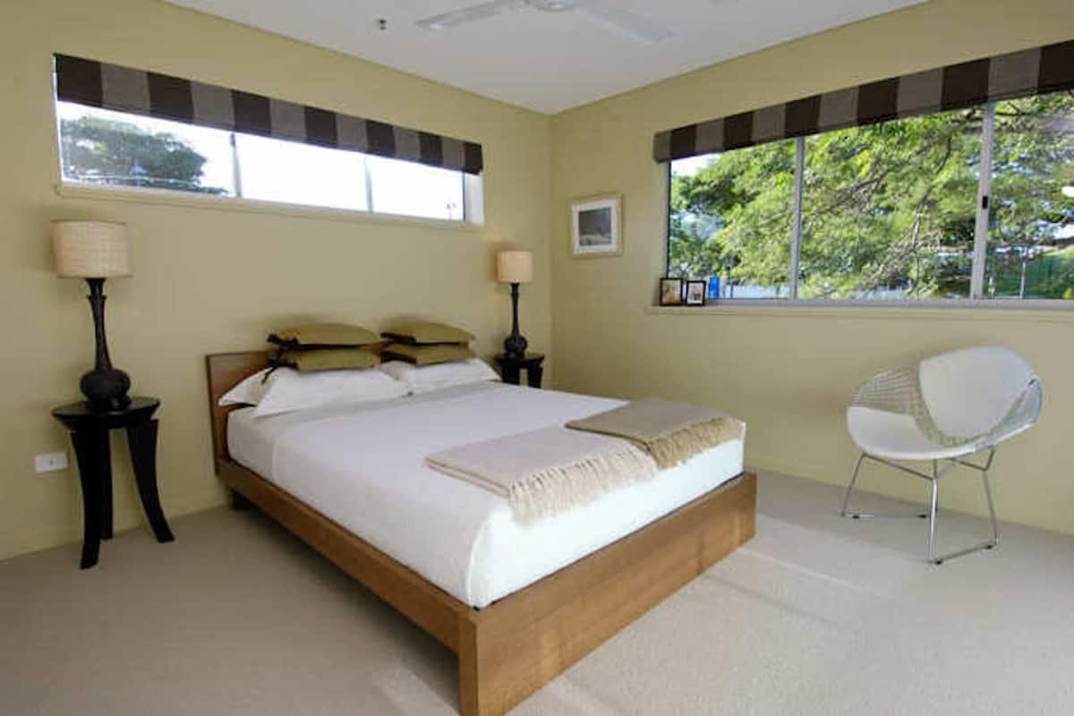 A bedroom with a bed, two bedside tables with lamps, a chair, and a window with blinds.