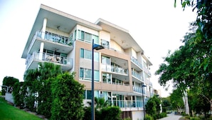 Un edificio residencial de varios pisos con balcones, un sendero y abundante vegetación.