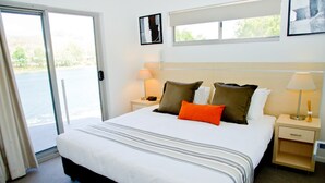 Una habitación de hotel con una cama grande, dos mesitas de noche, una ventana y una puerta que da a un balcón.