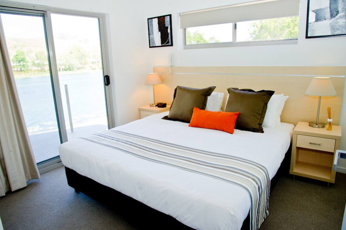 A hotel room with a large bed, two bedside tables, a window, and a door leading to a balcony.