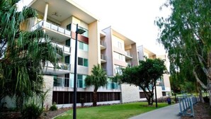 Un edificio residencial de varios pisos con balcones, rodeado de vegetación y un sendero.