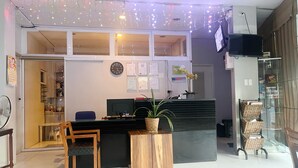 Zona de recepción con un escritorio de madera, una computadora, un reloj y una planta en maceta.