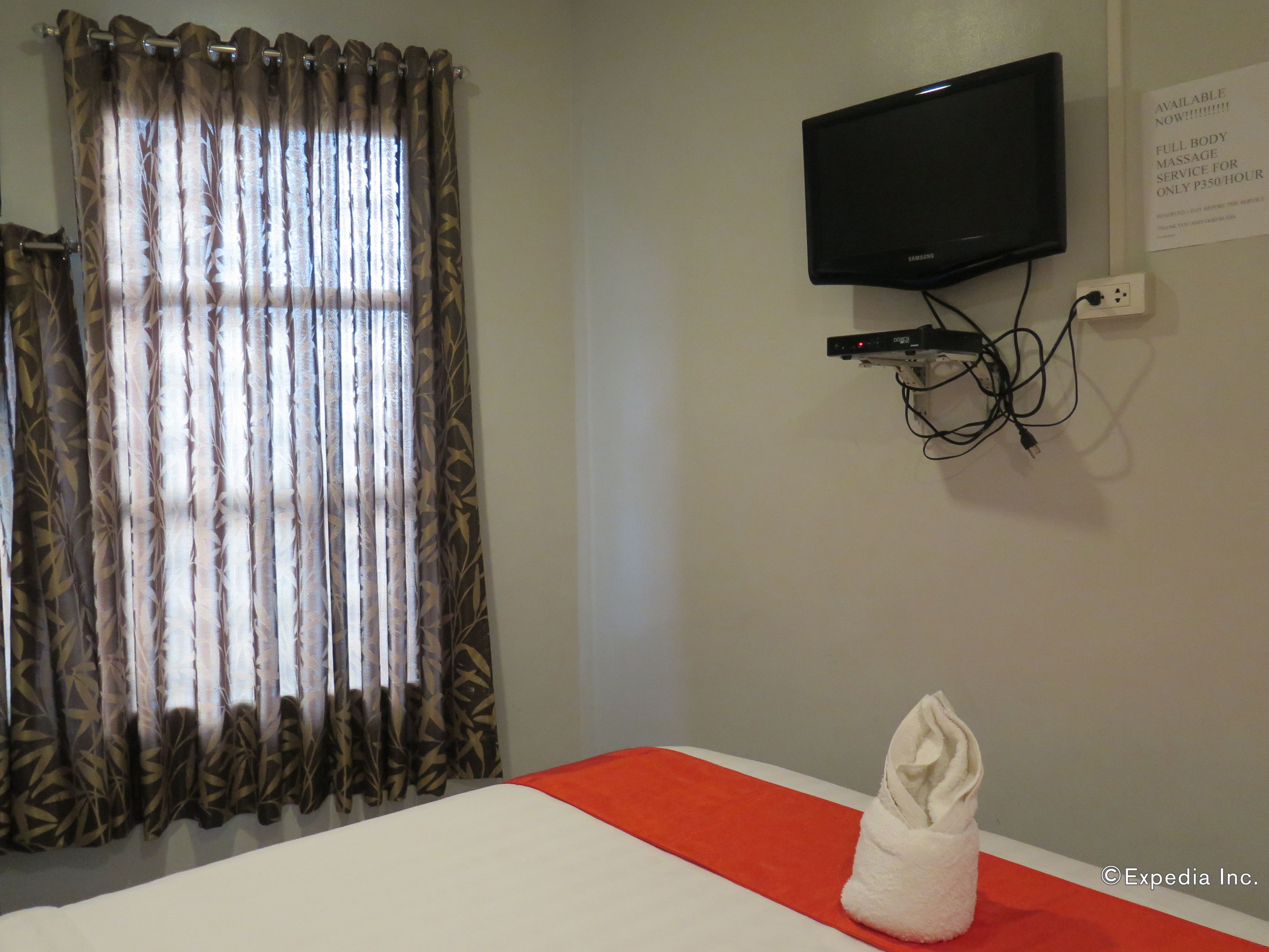 A hotel room with a bed, a TV mounted on the wall, and a sign indicating a massage service.