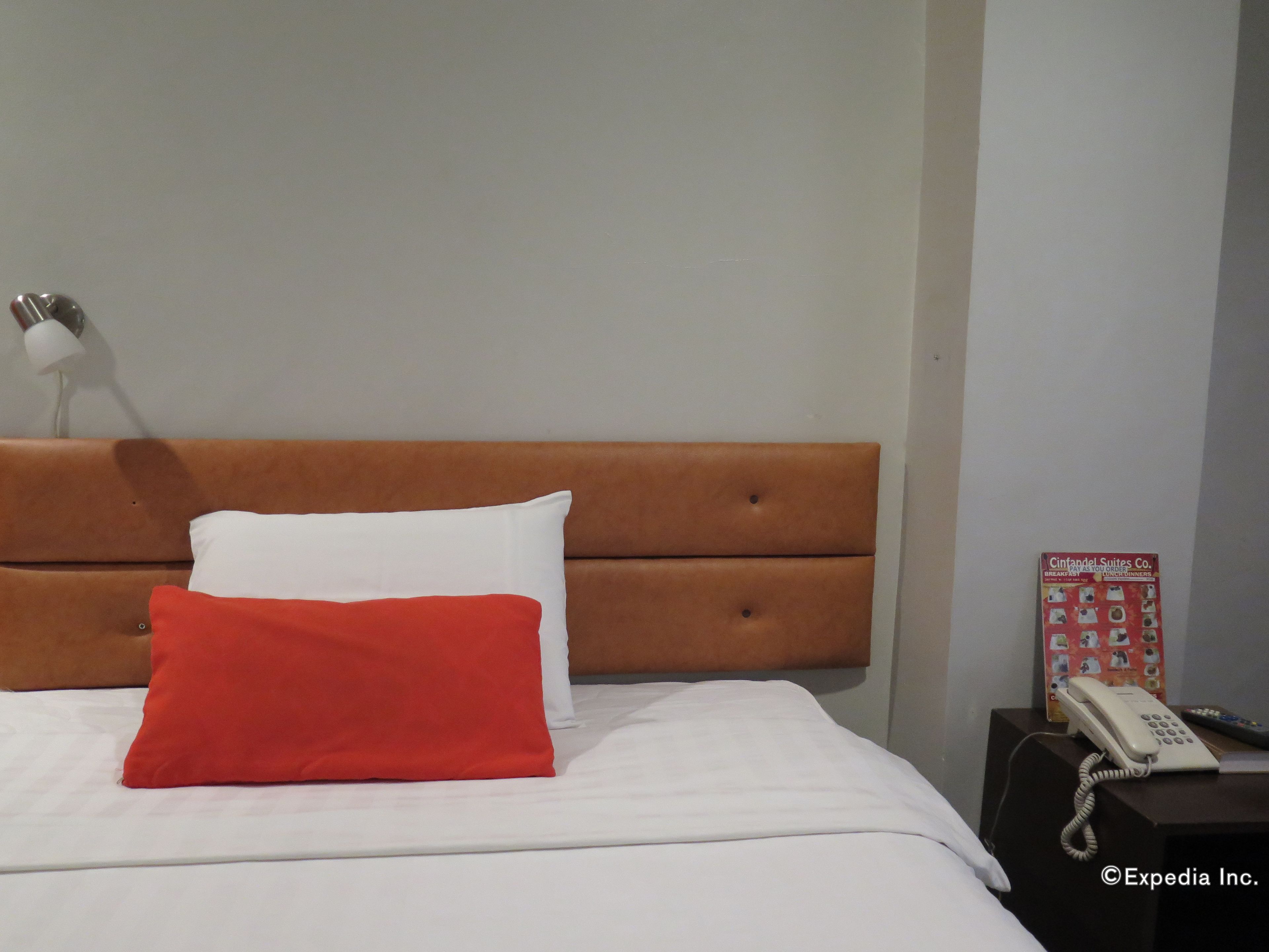 A hotel room with a bed, a red and white pillow, a white lamp, a telephone, and a menu on a table.