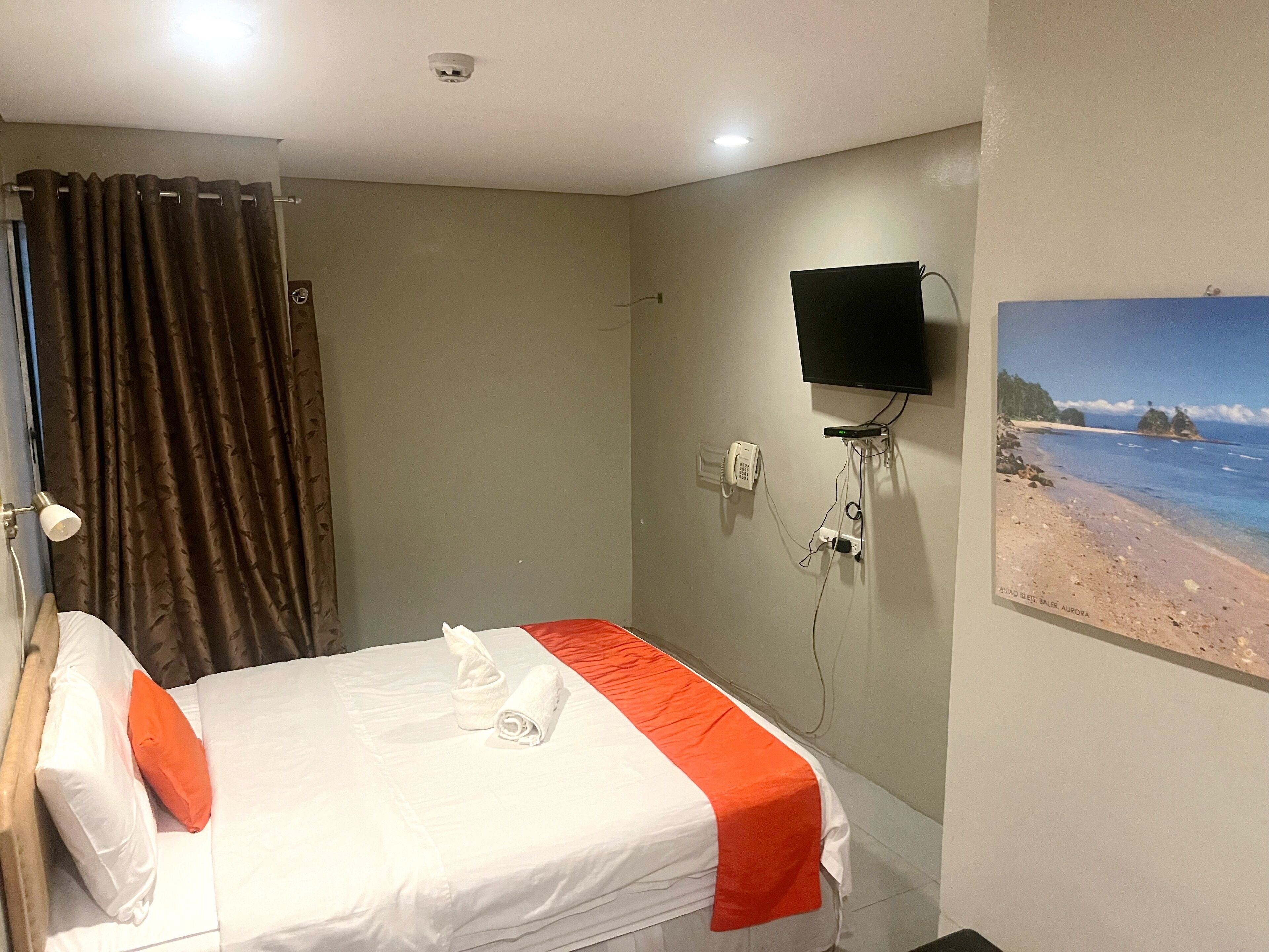 A hotel room with a bed, a television mounted on the wall, and a beach view poster.