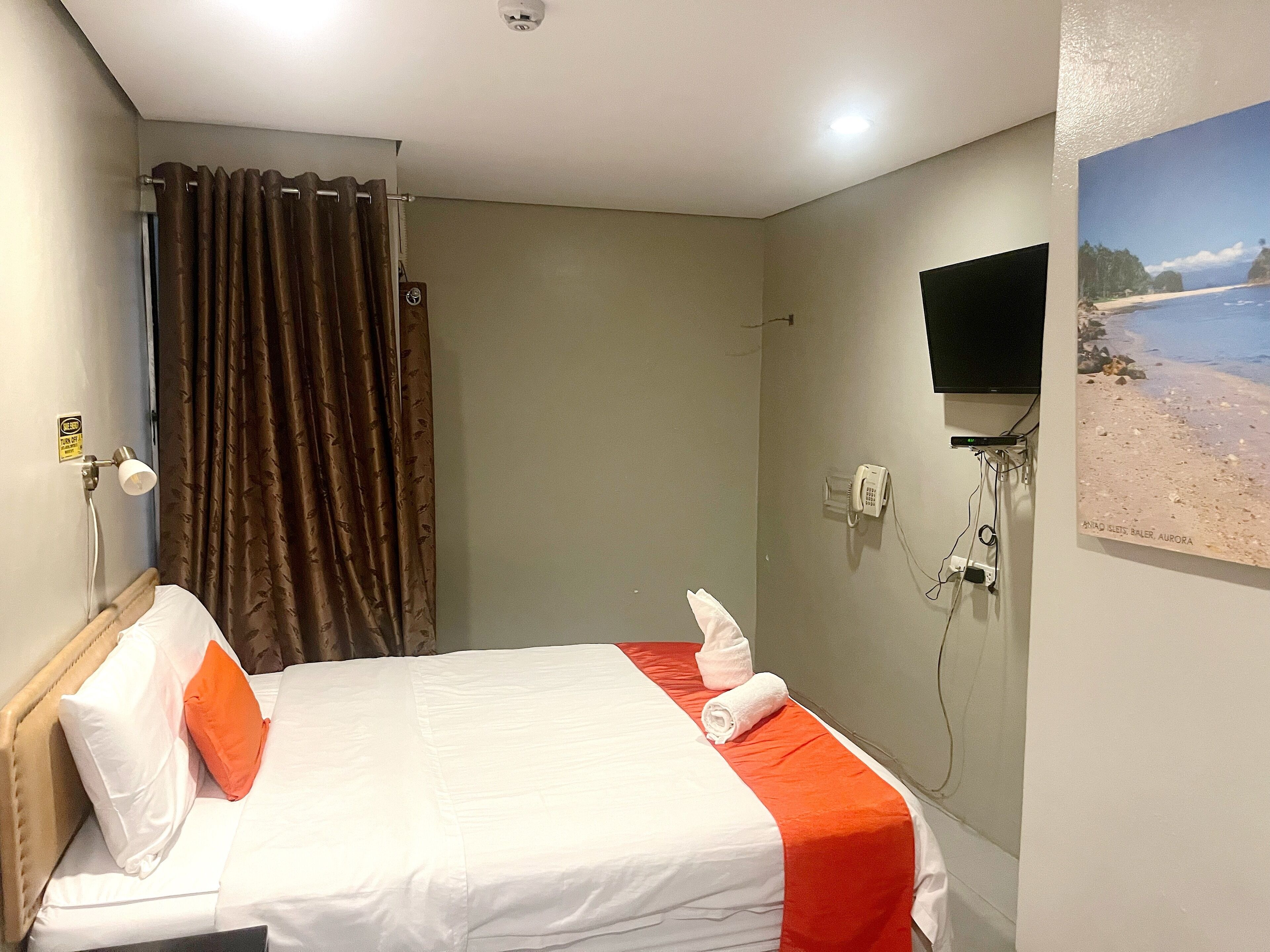 A hotel room with a bed, a shower curtain, a mounted TV, and a wall-mounted phone.