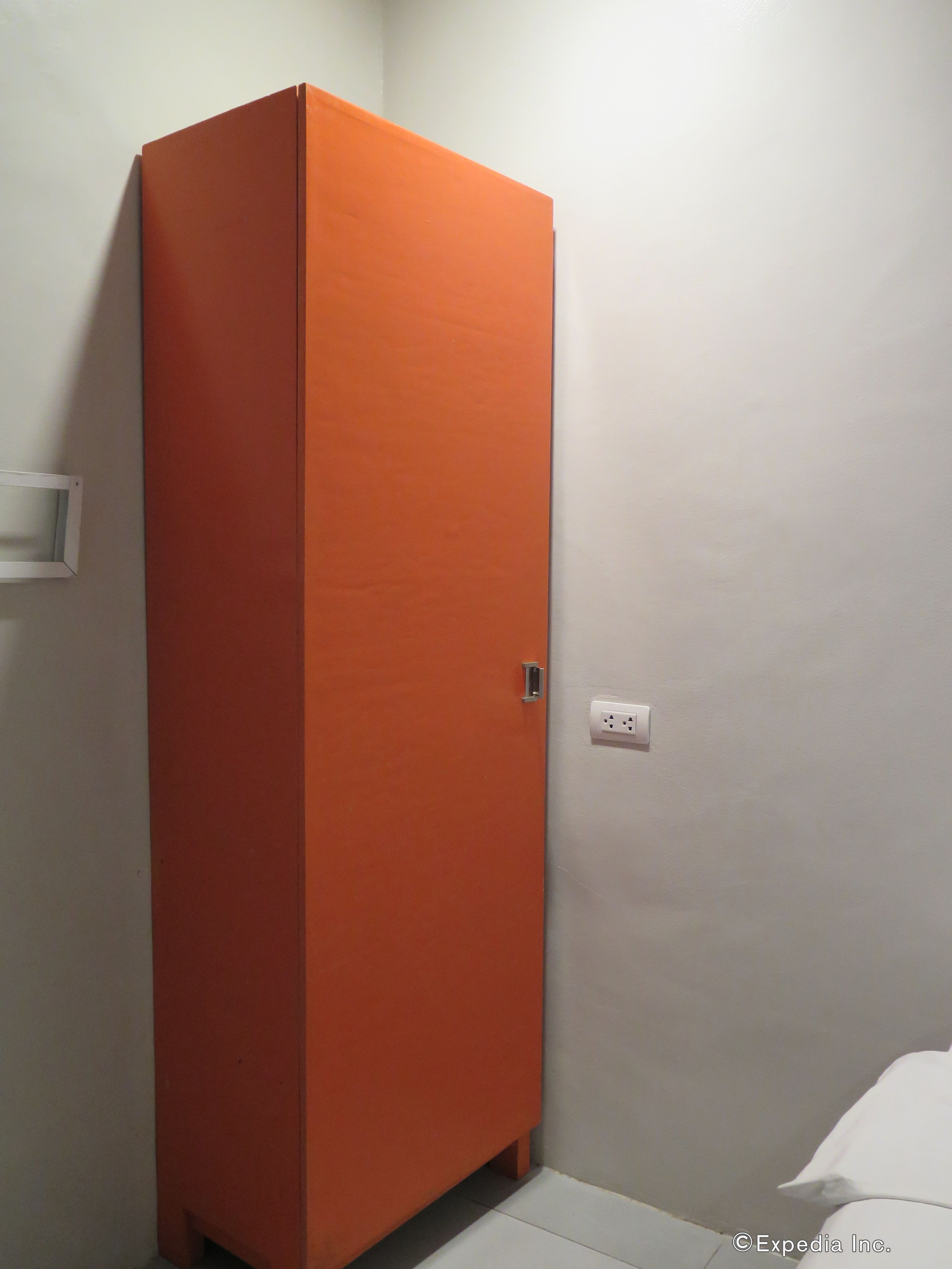 Ein Zimmer mit einem hohen, orangefarbenen Schrank an einer weißen Wand, einer weißen Steckdose und einem weißen Kissen auf dem Boden.