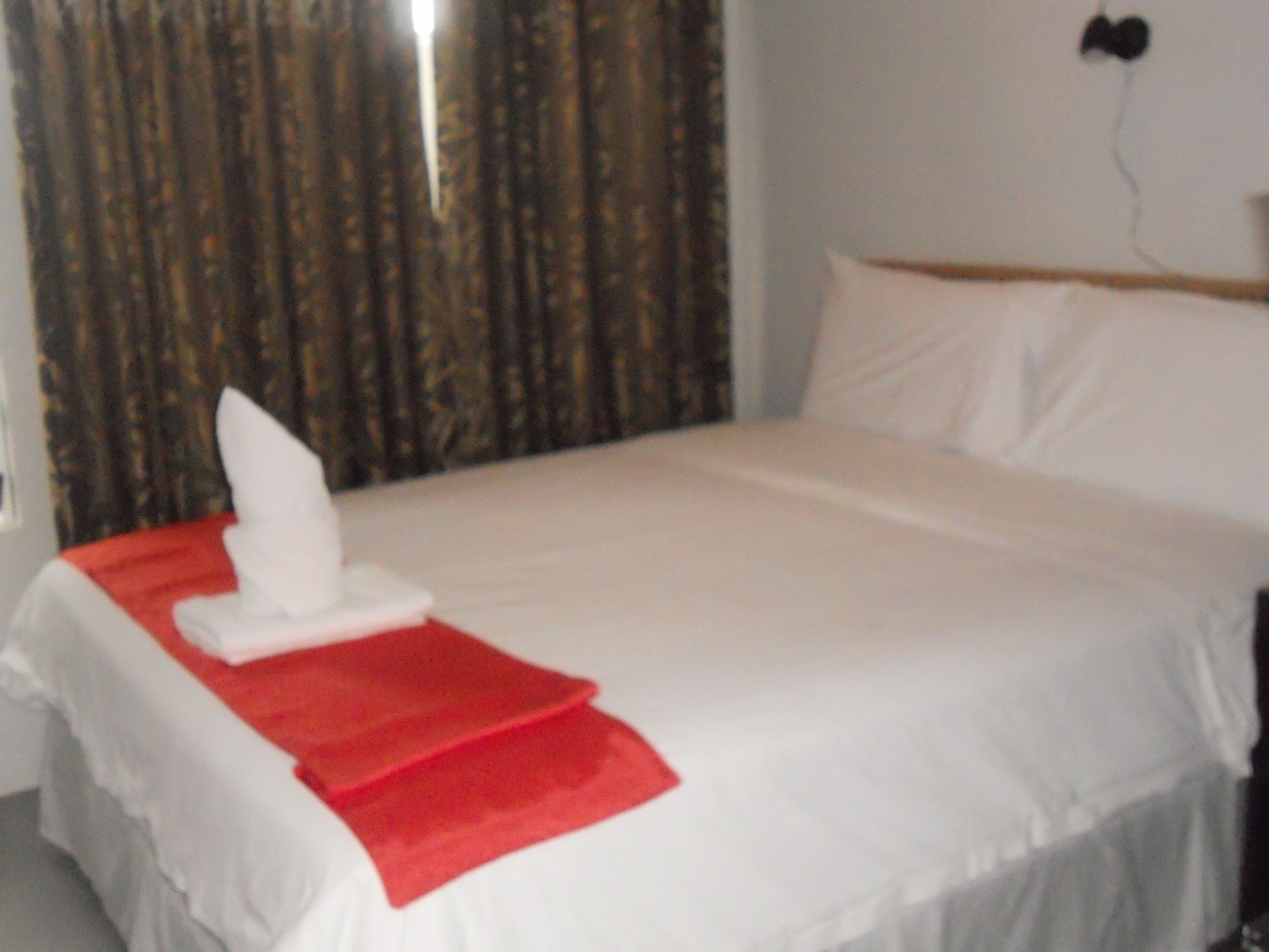 A hotel room with a neatly made bed, a red and white towel, and a curtain.