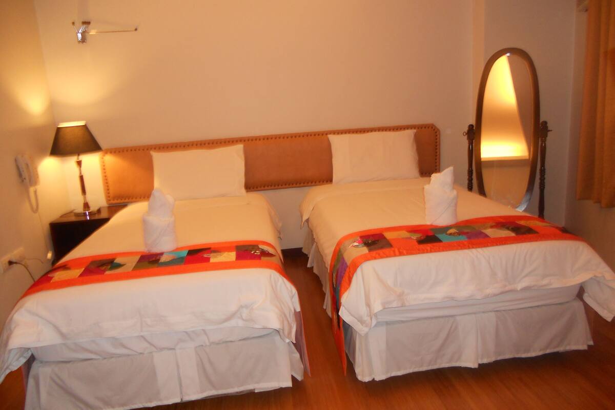Quarto de hotel com duas camas, mesa de cabeceira com abajur, espelho e telefone.