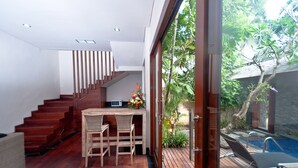 A modern interior with a wooden staircase, a dining area with a table and chairs, and a view of a swimming pool through a glass door. - The Dipan Resort Petitenget (Keroboken Kelod)