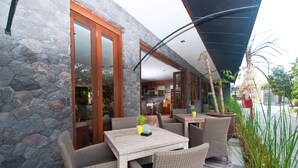 An outdoor seating area with wicker furniture, stone walls, and a view of the interior. - The Dipan Resort Petitenget (Keroboken Kelod)