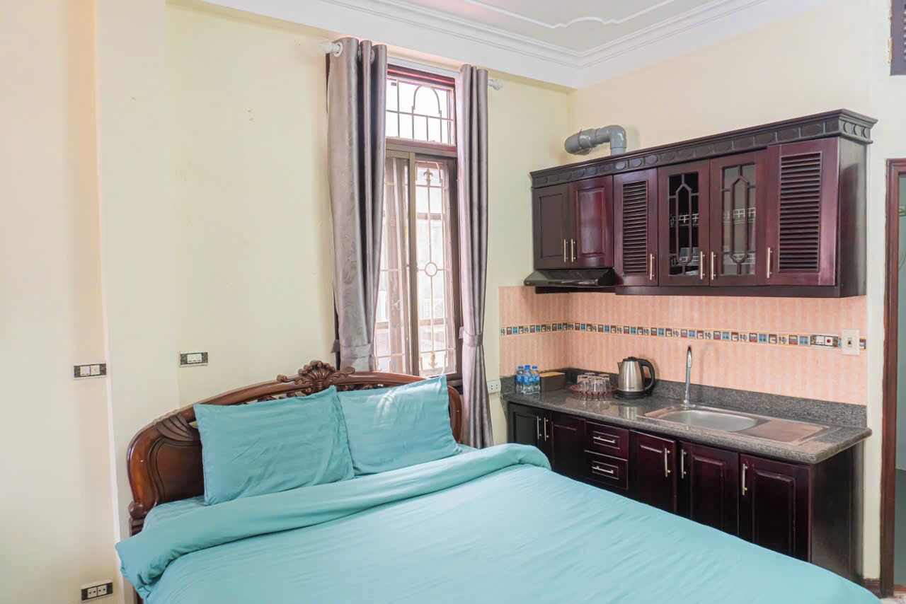 A bedroom with a bed, a window with curtains, a kitchen area with cabinets and a sink.