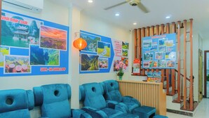 A hotel reception area with blue seating, a wooden reception desk, and walls decorated with travel posters. - Il Divo Hostel (Hanoi)