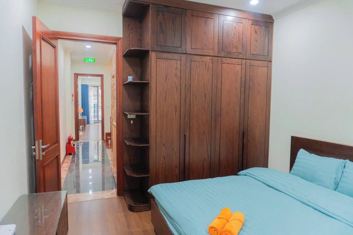 Una habitación de hotel con una cama, un armario de madera, una mesa de vidrio y un pasillo que conduce a otra habitación.