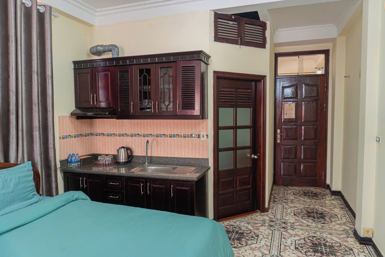 A compact hotel room with a kitchenette, a bed, a bathroom with a shower curtain, and a patterned floor.