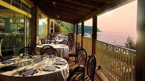 A dining area with tables set for a meal, overlooking a scenic view of the sea and hills. - Baia Tropea Resort (Parghelia)